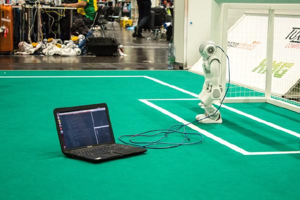 A robot connected to a computer on a soccer field.