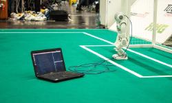 A robot connected to a computer on a soccer field.