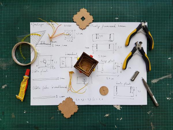 Tools, glue and piece of a prototyped box on a sheet of paper with drawing and dimensions
