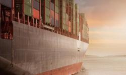 A container ship going towards the sunrise.