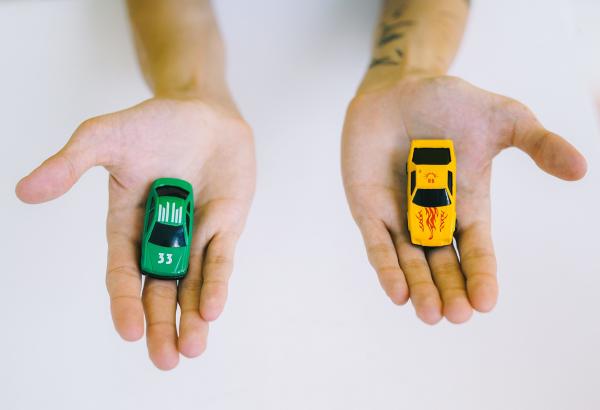 Free Pair of adult hands holding green and yellow toy cars on a white surface, symbolizing choice.